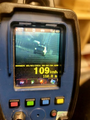 Zdjęcie kolorowe. Ręczny miernik prędkości z niewyraźnym zdjęciem pojazdu. Poniżej data 05/03/2026 i godzina 08:02:50.659. Na dole pomiar 109 km/h i odległość 106.0 m
