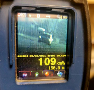 Zdjęcie kolorowe. Ręczny miernik prędkości z niewyraźnym zdjęciem pojazdu. Poniżej data 05/03/2026 i godzina 08:02:50.659. Na dole pomiar 109 km/h i odległość 106.0 m