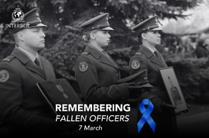 Zdjęcie czarno-białe. Troje funkcjonariuszy stoi obok siebie. Policjantka w głębi trzyma zdjęcie policjanta poległego w służbie. Policjantka  w środku trzyma policyjną czapkę służbową. Policjant trzyma medal. Wszyscy patrzą przed siebie. Na dole zdjęcia napis Remastering Fallen  Officer obiok granatowa wstęga.