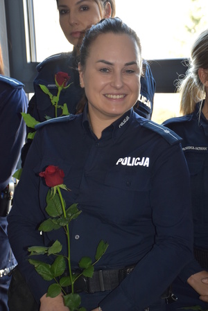 Zdjęcie kolorowe. Policjantka trzymająca czerwoną różę w dłoniach.