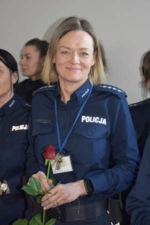 Zdjęcie kolorowe. Policjantka trzymająca czerwoną różę w dłoniach.
