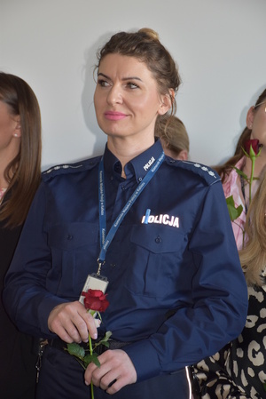 Zdjęcie kolorowe. Policjantka trzymająca czerwoną różę w dłoniach.