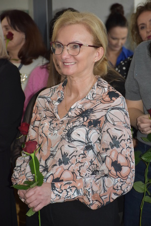 Zdjęcie kolorowe. Pracownica cywilna Policji trzymająca czerwoną różę w dłoniach.