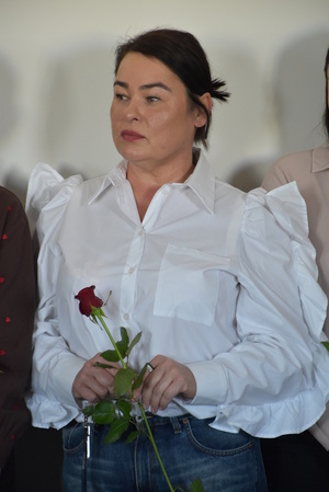 Zdjęcie kolorowe. Pracownica cywilna Policji trzymająca czerwoną różę w dłoniach.