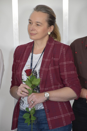 Zdjęcie kolorowe. Pracownica cywilna policji trzymająca czerwoną różę w dłoniach.