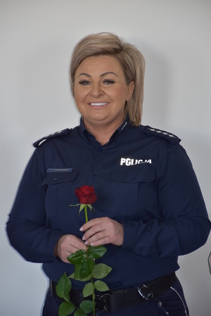 Zdjęcie kolorowe. Policjantka trzymająca czerwoną różę w dłoniach.