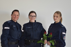Zdjęcie kolorowe. Trzy policjantki pozują do zdjęcie, dwie z nich trzymają czerwone róże w dłoniach.
