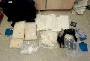 Zdjęcie kolorowe. Przeźroczyste woreczki strunowe z zawartością białej substancji rozłożone na podłodze. obok z prawej i lewej strony wagi elektroniczne, puste torby.