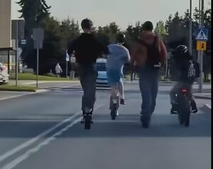 zdjęcie kolorowe, na zdjęciu cztery osoby, które jadą hulajnogami po jezdni