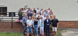Zdjęcie kolorowe. Grupa osób pozujących na schodach wejściowych przed budynkiem do wspólnego zdjęcia.