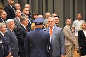 Policjant składa meldunek ministrowi podczas uroczystej zbiórki z okazji święta policji. Z lewej strony stoją zaproszeni goście.