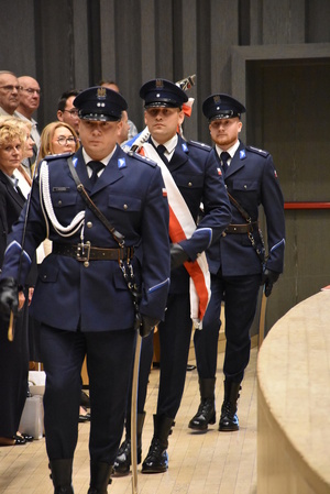 Poczet sztandarowy (trzech policjantów) wchodzi na aulę podczas uroczystej zbiórki.