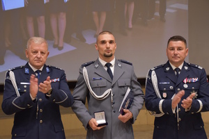 Trzech policjantów stojących na scenie. Środkowy trzyma w dłoni "Kryształową Gwiazdę" wyróżnienie nadawane wielkopolskim policjantom.
