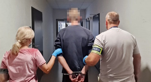 Zdjęcie kolorowe. Dwójka nieumundurowanych policjantów prowadzi zatrzymanego, który ma ręce skute kajdankami. Zdjęcie robione z tyłu.