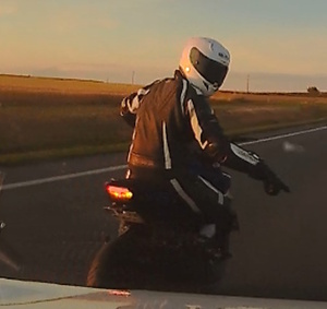 Motocyklista jadący na motocyklu. Ręką wskazuje, żeby się zatrzymać.